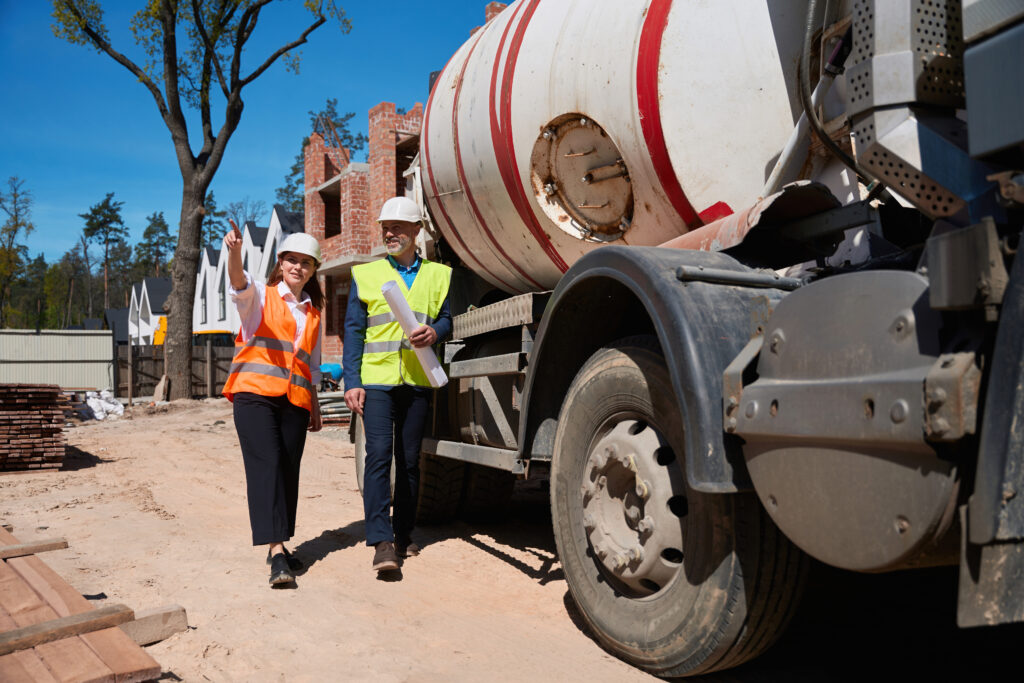 Two workers in hard hats walking beside a concrete mixer truck at a residential building site